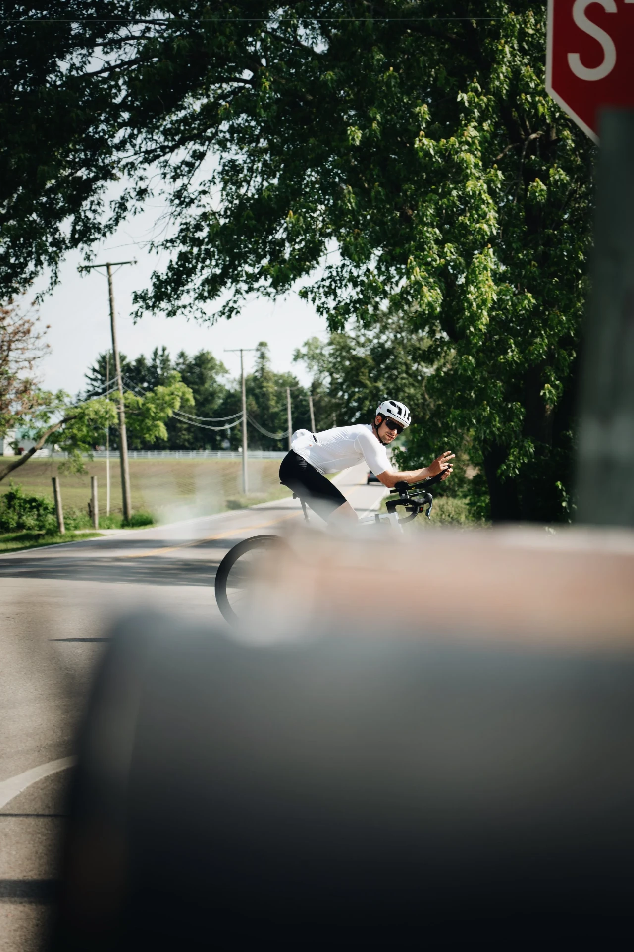 Peter Bolliger riding past a stop sign on a tree-lined road