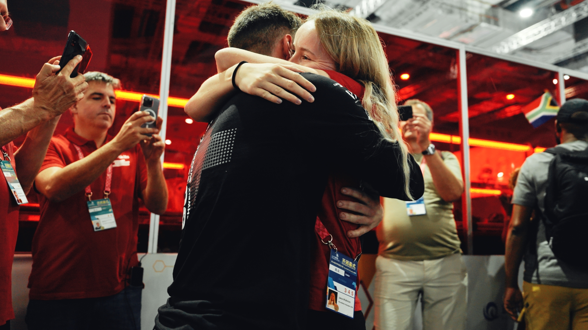 Two people embracing at a ceremony, crowd photographing